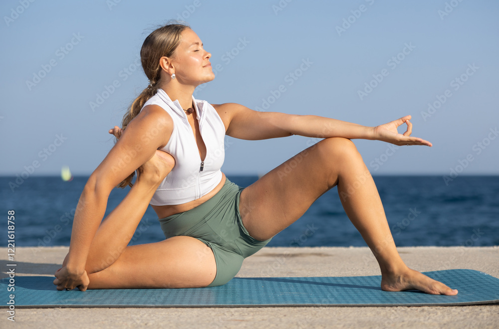 Young girl in sportwear doing stretching exercises for strong arms and abs and difficult yoga asana on the seashore on a sunny day Young girl in sportwear doing stretching exercises for strong arms and abs and difficult yoga asana on the seashore on a sunny day