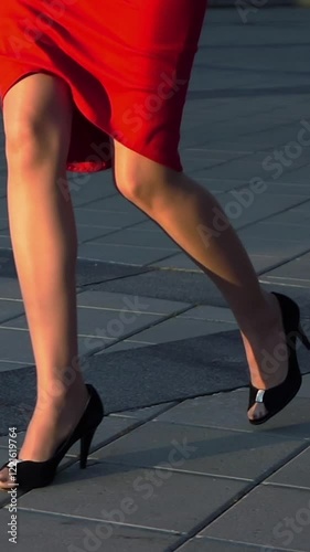 Sexy woman legs in black high heels shoes walking near glass business centre. Steadicam shot. Slow motion. Red suit, spectacles. Cinematic teal and orange sunrise shooting. Vertical Shot.
