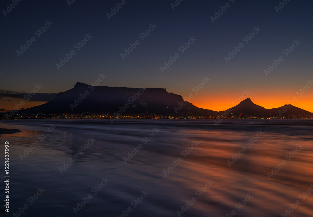 Long exposure shot of Table Mountain silhouette with Cape Town lit up after sunset, viewed from Sunset Beach, South Africa