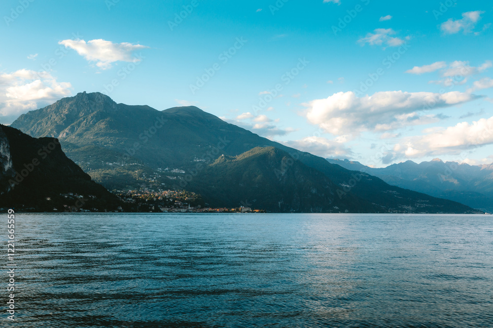 Tranquil Lake Como reflecting blue sky with majestic mountains and charming village nestled along the shoreline, creating a picturesque scene in Lombardy, Italy Tranquil Lake Como reflecting blue sky with majestic mountains and charming village nestled along the shoreline, creating a picturesque scene in Lombardy, Italy