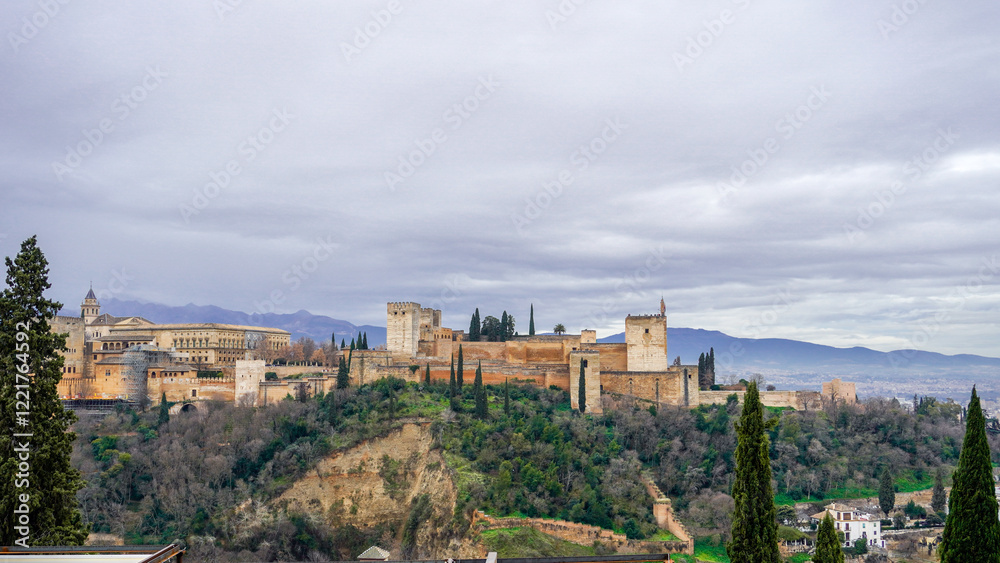 Obraz premium A majestic Moorish palace perched atop a hill, overlooking the city of Granada. The Alhambra's intricate architecture and stunning gardens are a testament to the rich history of Al-Andalus. The image 