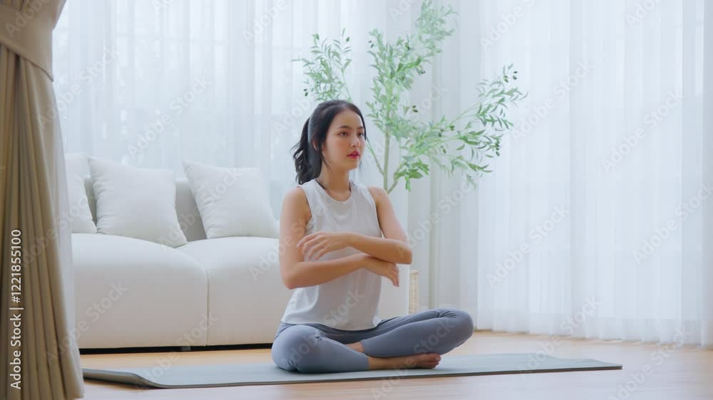 Happy young Asian woman practicing yoga and meditation at home sitting on floor in living room in lotus position and relaxing with closed eyes. Mindful meditation and wellbeing concept Happy young Asian woman practicing yoga and meditation at home sitting on floor in living room in lotus position and relaxing with closed eyes. Mindful meditation and wellbeing concept