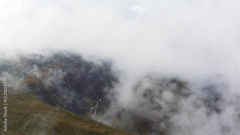 Dramatic view of mountain valley surrounded by mist, grassy terrain, and a winding glacial stream. Dramatic view of mountain valley surrounded by mist, grassy terrain, and a winding glacial stream.
