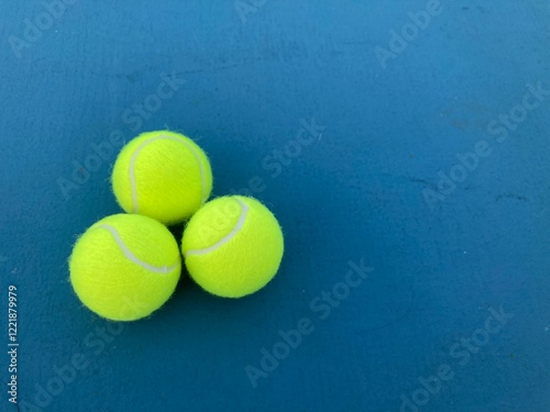 top view shot of three tennis balls on a blue tennis court with the copy space on the right side of frame