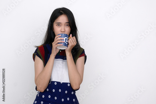 A young woman wearing an apron drinks from a blue cup; serious expression photo