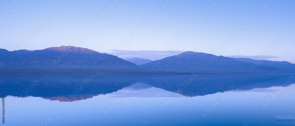 Fototapeta premium Soft blue clouds and mountains reflected in water at dawn. Made with generative AI