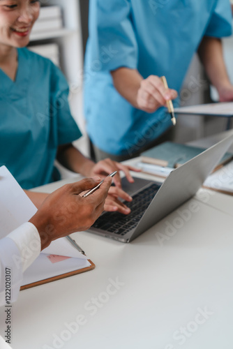 Two male doctors and a female nurse meet at a table in the hospital, collaborating on medical tasks, using laptops and computers, showcasing teamwork,and focusing on health,medicine,and patient care
