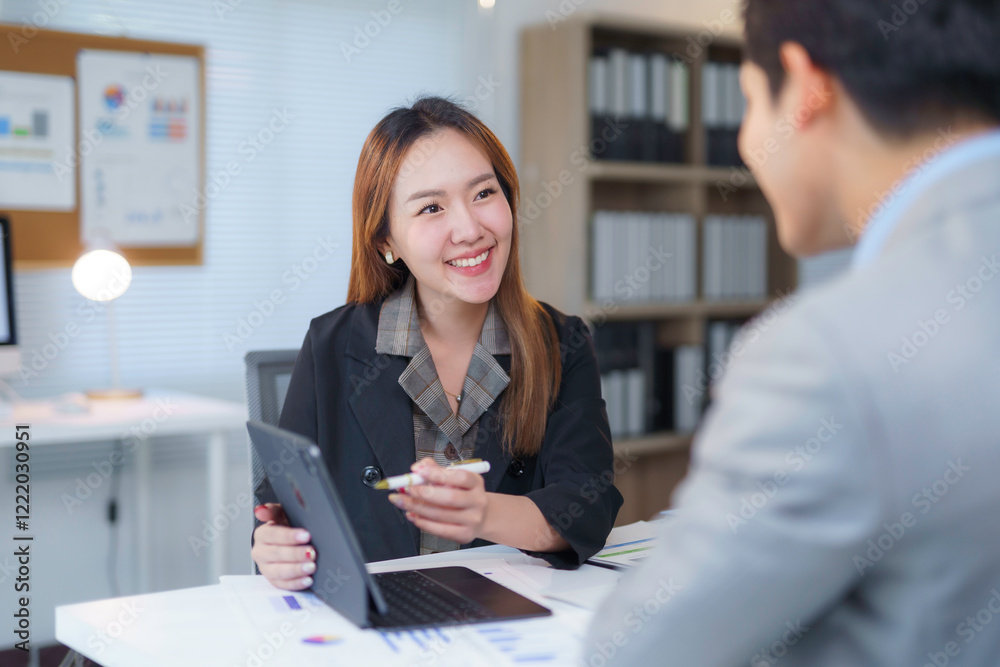 Obraz premium Asian businesswoman showing marketing data on tablet to businessman in office