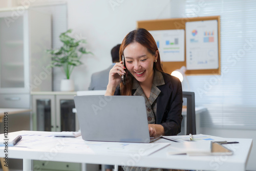 Asian businesswoman working with laptop and talking on phone in modern office