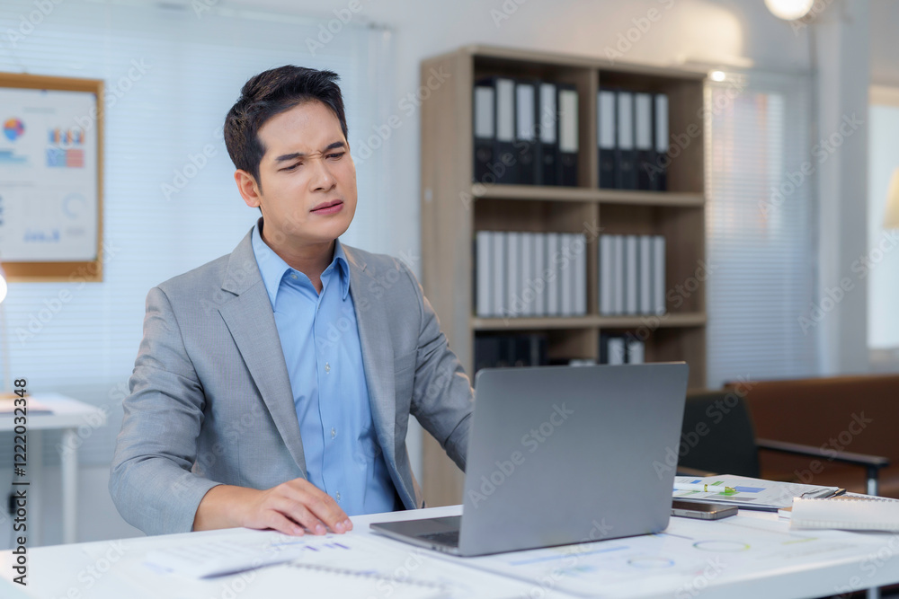 Fototapeta premium Stressed Asian businessman having neck pain while working on laptop in office