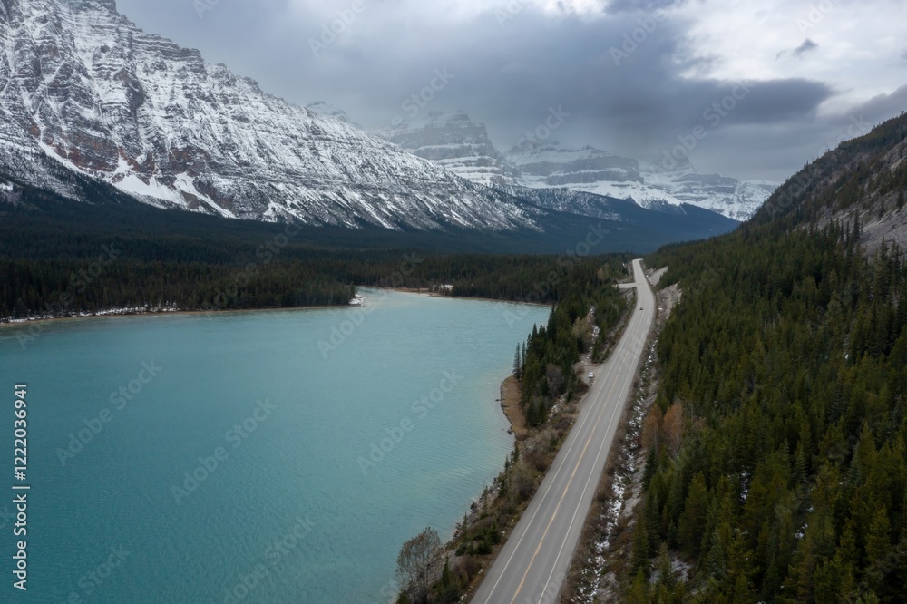 Obraz premium Snowy mountain range, a tranquil lake, and a highway winding through the forest. A scenic drive through the Canadian Rockies. Waterfowl Lake, Banff National Park, Alberta, Canada