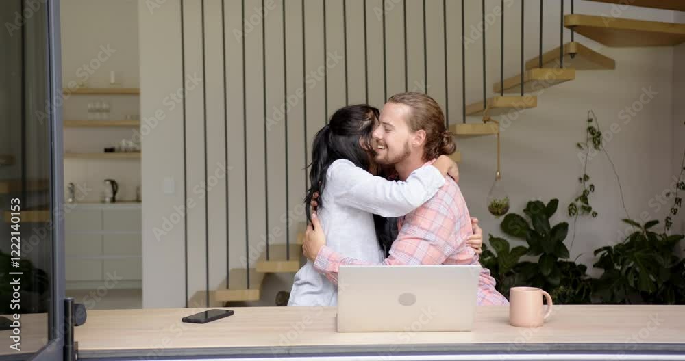 A biracial young woman and Caucasian young man sit with laptop in kitchen at home A biracial young woman and Caucasian young man sit with laptop in kitchen at home