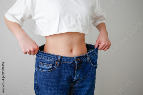 A teenage girl in huge jeans on a gray background. Weight loss. Diet in adolescence.
