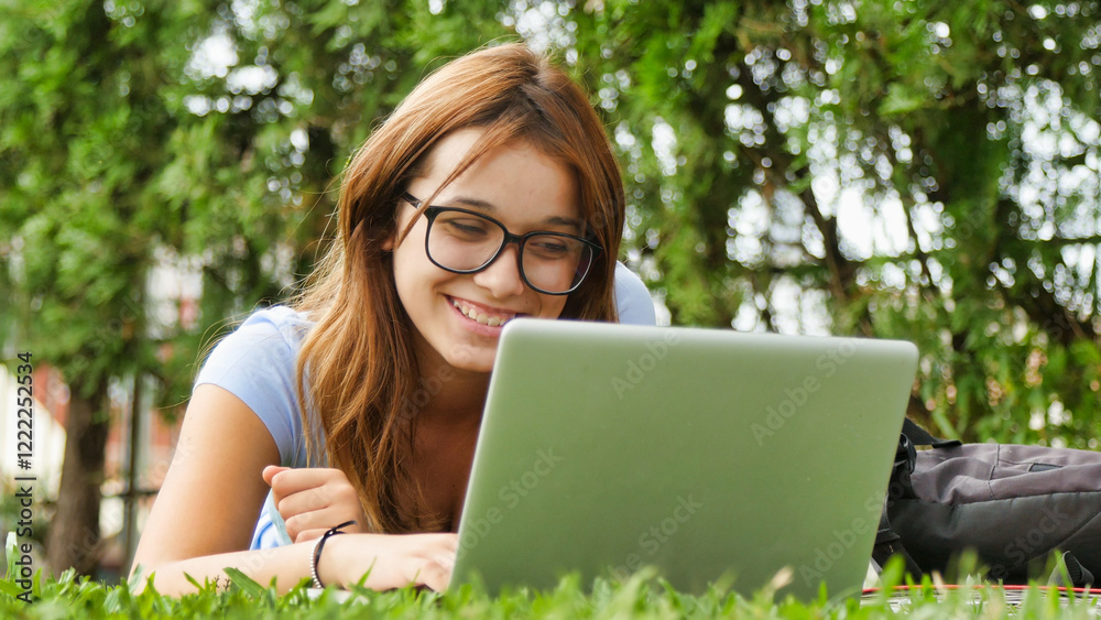 Caucasian teenager girl lying on the grass using laptop. Happiness and lightheartedness concept Caucasian teenager girl lying on the grass using laptop. Happiness and lightheartedness concept