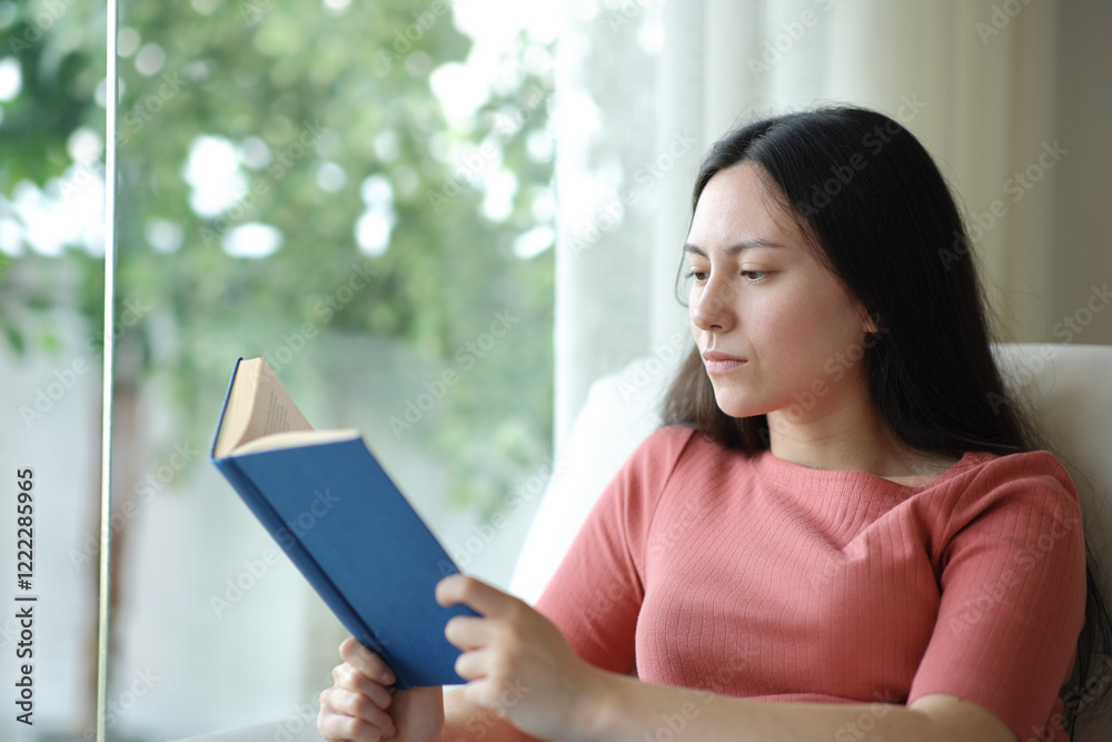 Serious asian woman reading a paper book on a sofa at home Serious asian woman reading a paper book on a sofa at home