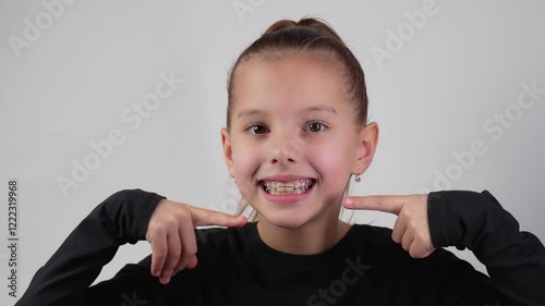 Happy child with dental braces showing thumbs up gesture smiling . Little girl with teeth retainers, smiling, looking at camera, close-up. Child with orthodontic plate on a white background
