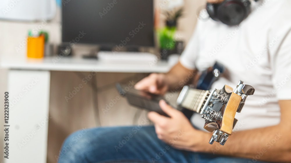 A young man with a smartphone while holding an electric guitar at home. A young man with a smartphone while holding an electric guitar at home.