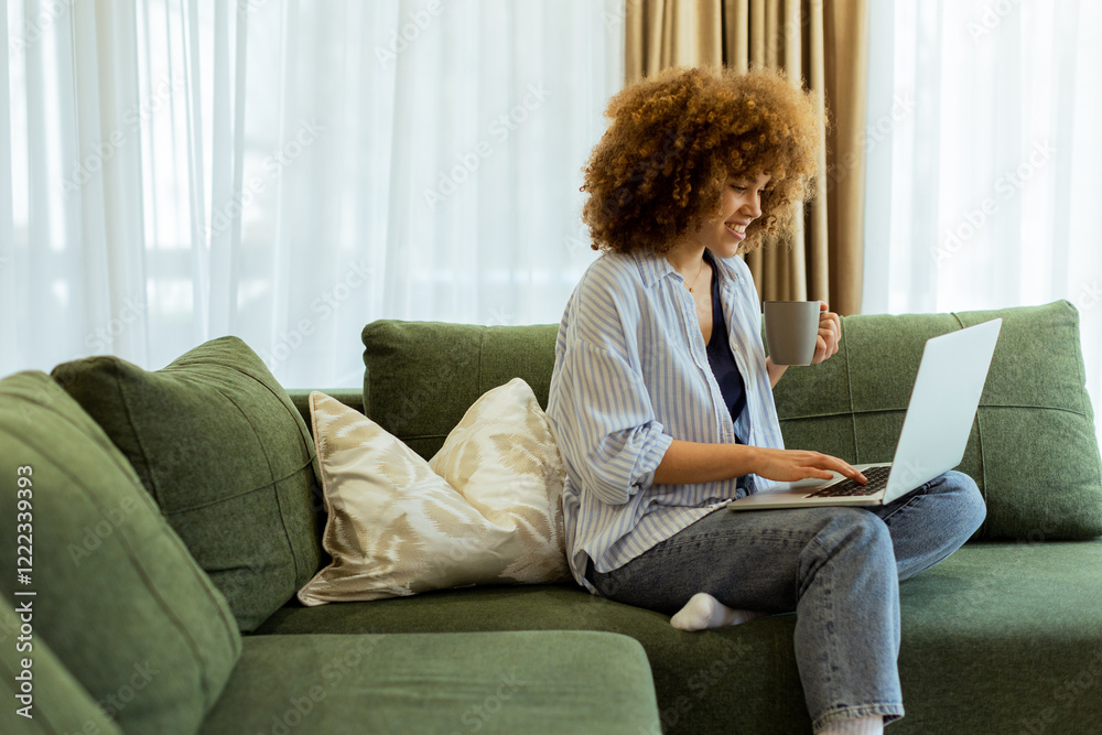 Fototapeta premium Young woman enjoying a cozy morning with coffee and a laptop in a bright and airy living room