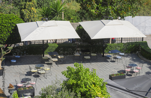 Outdoor dining area with shaded tables, surrounded by greenery and trees in a tranquil setting during the daytime