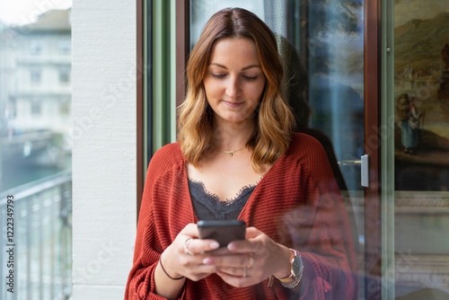 Young woman using cell phone at the balcony door photo