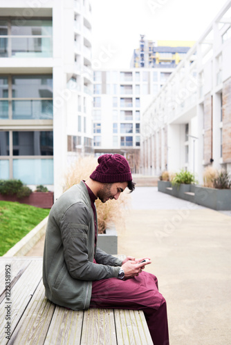 Side view of bearded guy in purple hat and clothes browsing mobile phone sitting on bench photo