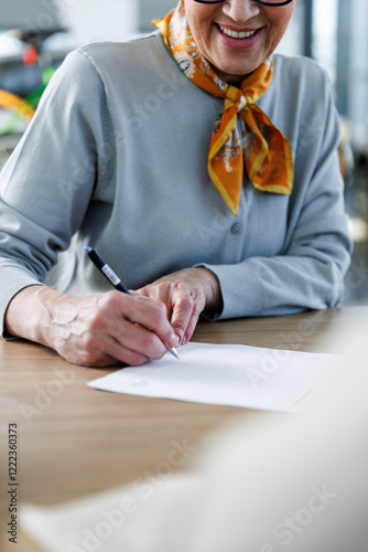 Smiling senior woman signing sales contract at desk photo