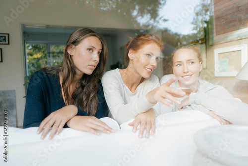 Mother with two teenage girls on couch at home behind windowpane photo