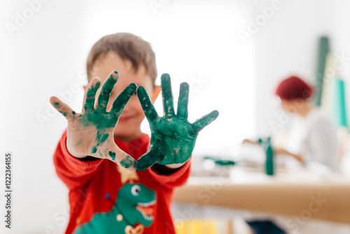 Boy showing his hands painted green while doing crafts at home photo