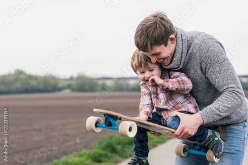 Father and son having fun, playing with skateboard outdoors photo