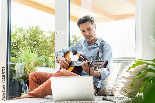 Mature man practising on the guitar, using laptop and earphones photo