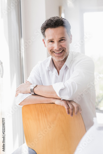 Mature man sitting on chair backwards, smiling photo