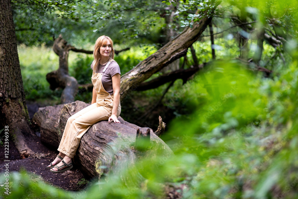 Smiling woman sitting on tree trunk in forest Smiling woman sitting on tree trunk in forest
