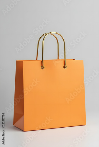 Bright orange shopping bag with gold handles on light grey background is a versatile template for showcasing branding or product design. Stylish and minimalistic look.