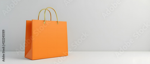 Bright orange shopping bag with gold handles on light grey background is a versatile template for showcasing branding or product design. Stylish and minimalistic look.