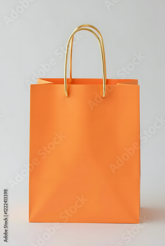Bright orange shopping bag with gold handles on light grey background is a versatile template for showcasing branding or product design. Stylish and minimalistic look.