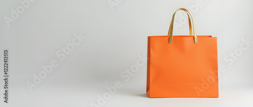 Bright orange shopping bag with gold handles on light grey background is a versatile template for showcasing branding or product design. Stylish and minimalistic look.