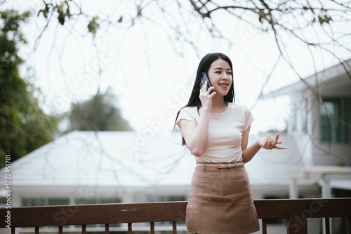 A smiling young woman is enjoying a relaxing day in a green city park, using her smartphone to work or relax. She is surrounded by nature. She works remotely while living a modern and active life. photo