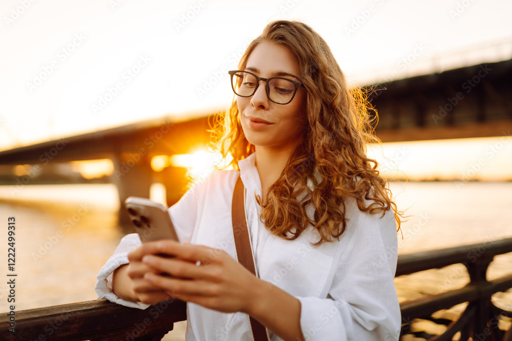 Fototapeta premium A young caucasian woman using her smartphone while walk on embankment. Concept of vocational, blogging, technology, weekend.
