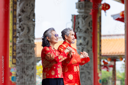 Asian marriage senior couple in cheongsam qipao dress is making wish to ancestral god inside Chinese Buddhist temple during lunar new year for best wish blessing and good luck photo