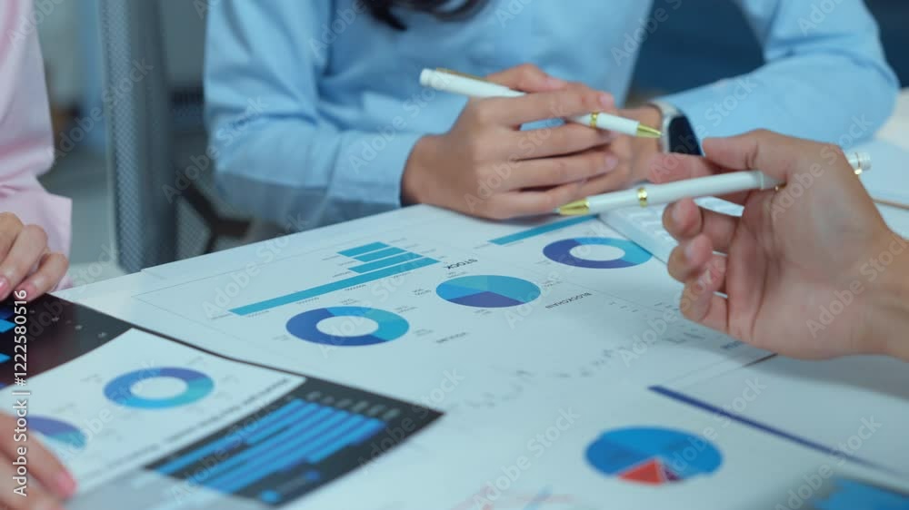 Professional business team reviewing financial data, pointing at performance charts with pens, analyzing strategic metrics in corporate meeting setting
