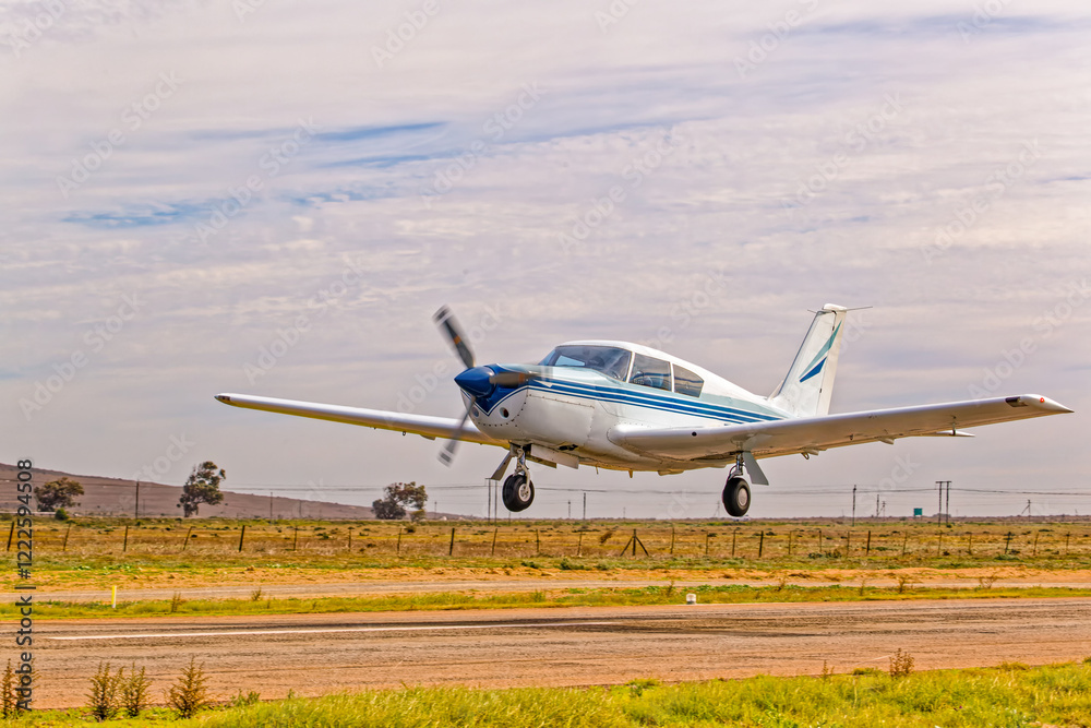 Classical style blue and white single engine aircraft with four seats taking off from airstrip in the Western Cape, South Africa Classical style blue and white single engine aircraft with four seats taking off from airstrip in the Western Cape, South Africa