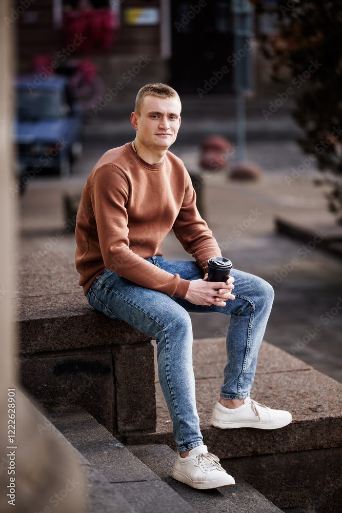 Fototapeta premium Young man sitting on steps with coffee cup in casual attire