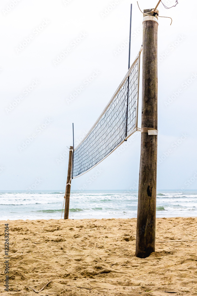 Beach volleyball net on sandy shore with ocean waves in background