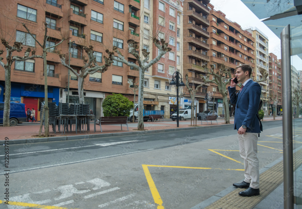 Fototapeta premium Businessman is waiting for the bus and talking on his phone 