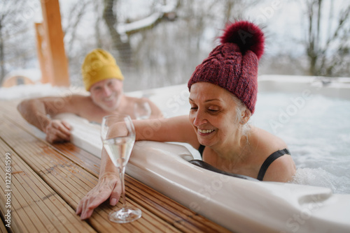 Lovely seniors drinking champagne while bathing in hot tub during. Romantic wellness getaway with spa during Valentine's weekend. photo