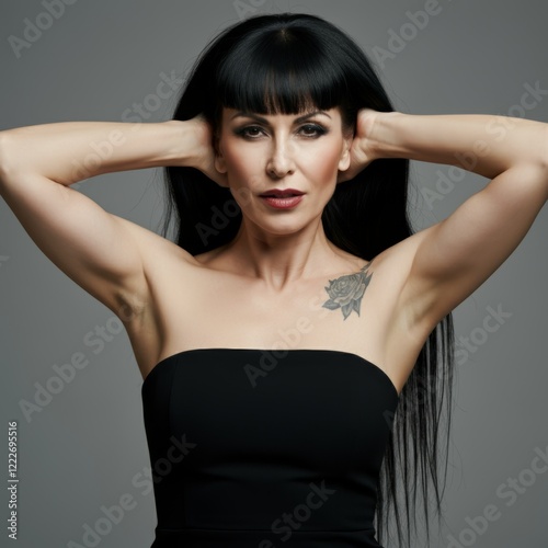 Elegant woman with tattoo and long black hair posing in strapless dress