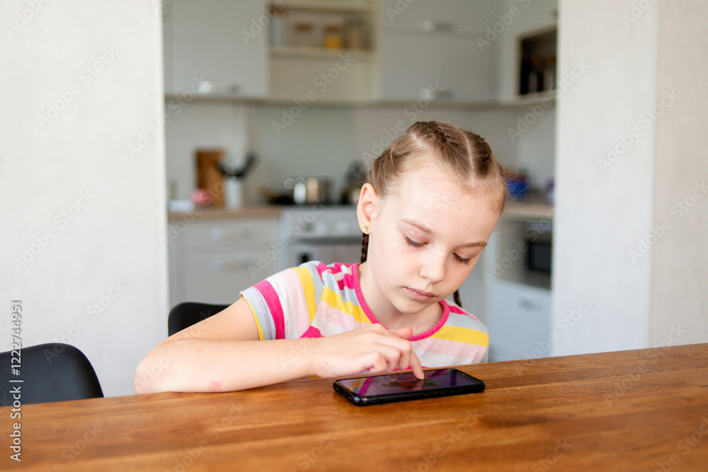 Little girl playing with smartphone while sitting at table in kitchen Little girl playing with smartphone while sitting at table in kitchen
