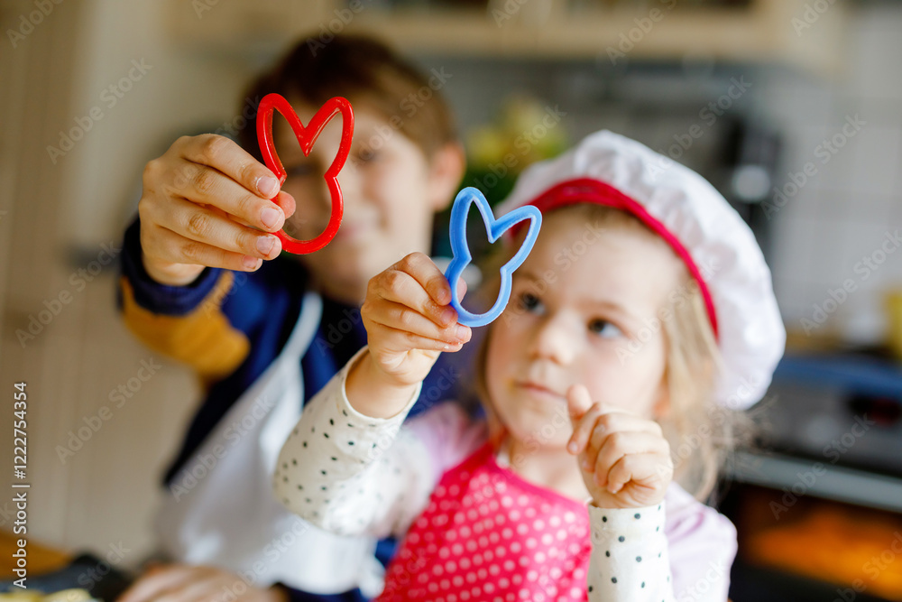 Cute little toddler girl and preteen kid boy baking Easter cookies at home indoors. Children, siblings with apron and chef hat cut out bunny cookie in domestic kitchen. Brother and sister in love