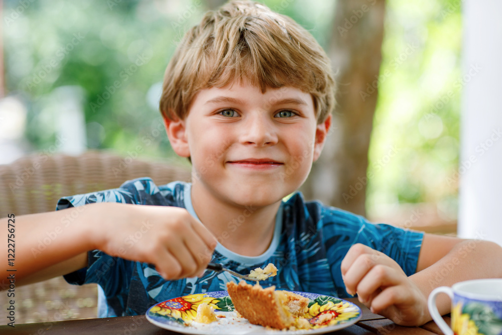 Beautiful kid boy eating apple pie in restaurant on vacations. Happy healthy child in an outdoor cafe in summer time, eating cake Beautiful kid boy eating apple pie in restaurant on vacations. Happy healthy child in an outdoor cafe in summer time, eating cake
