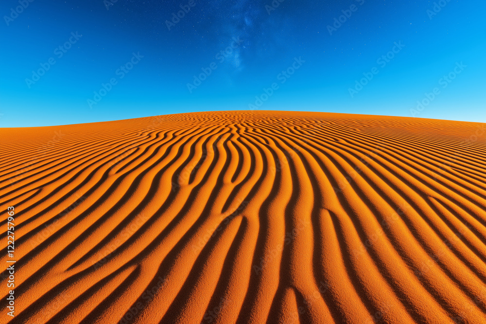 Naklejka premium Rippled sand dunes in a desert glowing under a vibrant blue sky with faint stars at dusk